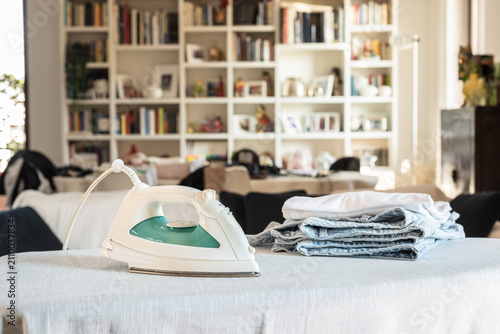 Modern iron on ironing board with clothes at home.