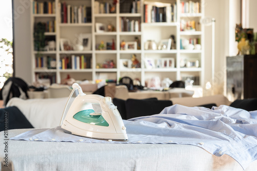 Modern electric iron on a shirt on ironing board at home.