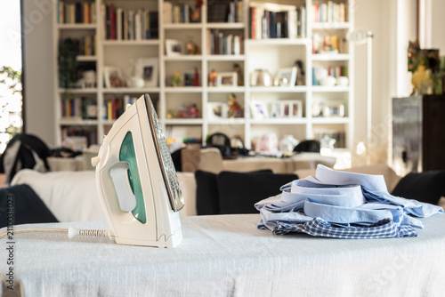 Modern iron on ironing board with clothes at home.