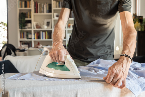 Front view of a man ironing shirt at home on sunny day.