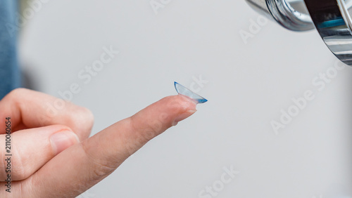 Obraz na płótnie Close-up of a teenager's hand holding a blue contact lens on the fingertip, with