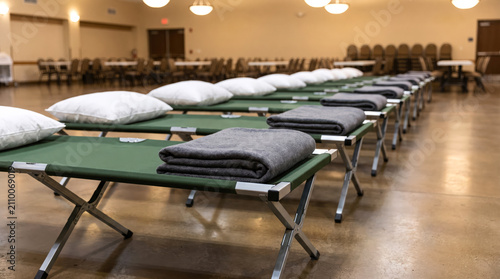 Temporary shelter provides orderly beds with pillows and blankets. Emergency accommodation facility prepares sleeping spaces for displaced residents. Crisis response concept.