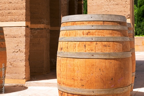 Fotografia Close up of vintage wooden wine barrel with metal hoops on rammed earth building