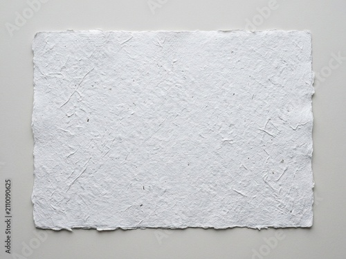 A sheet of handmade white paper with a rough, textured surface and deckled edges, centered on a neutral grey background