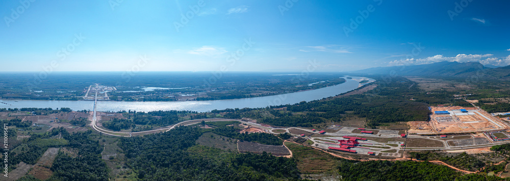 Fototapeta premium Drone perspective of the Fifth Thai Lao Friendship Bridge spanning tranquil river waters and rural landscapes, highlighting transportation infrastructure and regional development.