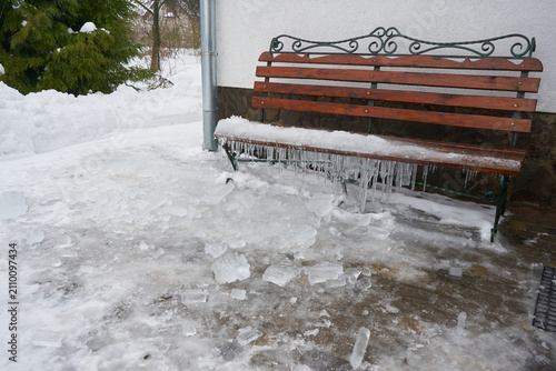 Wooden garden bench with long icicles hanging from the frozen seat, Frozen wooden bench covered with snow and ice in the backyard in winte