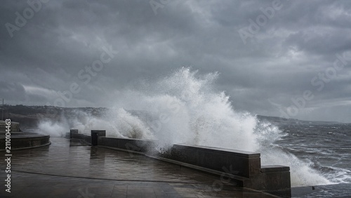 Powerful Storm Surge Waves Crashing Against Coastal Promenade During Extreme Weather Along the Ocean Shoreline