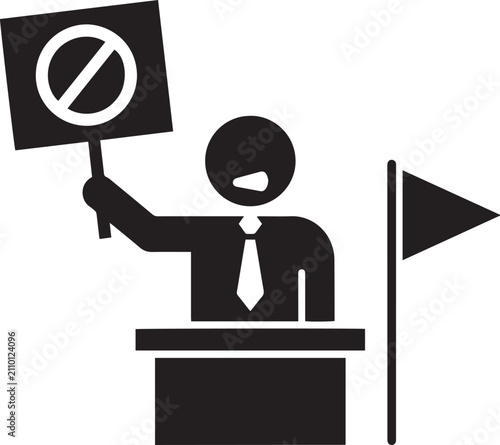 A protestor holding a sign with a prohibition symbol, standing at a podium with a flag beside him