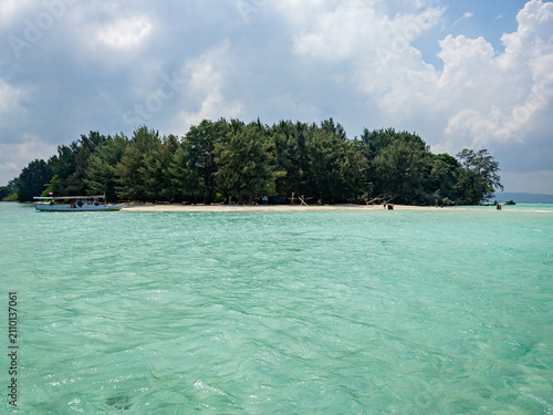 Tour boat arriving at a remote Gleyang Island beach, Karimunjawa National Park, Jepara, Jawa Tengah, Indonesia, showing clear turquoise water and lush green trees under a cloudy sky