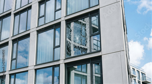 Shattered glass window pane on modern office building facade. Broken building exterior wall showing damage and vandalism. Urban architecture safety hazard, repair and maintenance concept.
