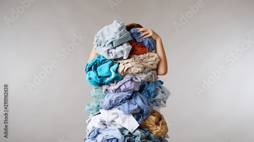 Woman overwhelmed by enormous pile of dirty laundry and clothes, struggling with household chores, feeling tired and stressed by cleaning routine