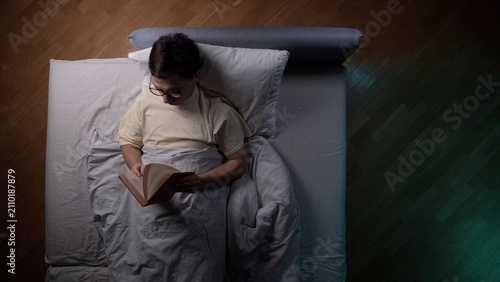Obraz na plátne Man wearing glasses deeply engrossed in a book, finding peace and relaxation whi