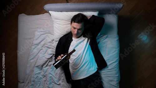 Obraz na plátně Young man lying on his back in bed, dressed in a t shirt and shirt, holding an e