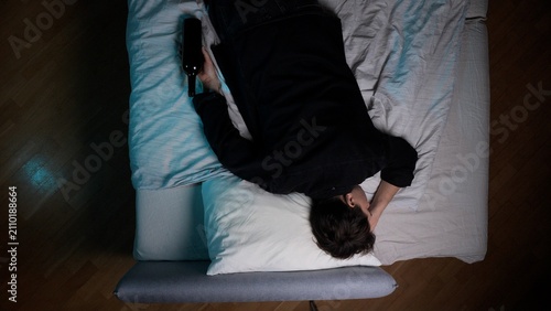 Принти на полотні Young man experiencing addiction and depression, lying in bed holding a dark bot