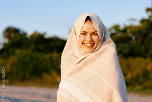Quadro su tela Smiling woman wrapped in a light shawl on a sunny beach, warm breeze