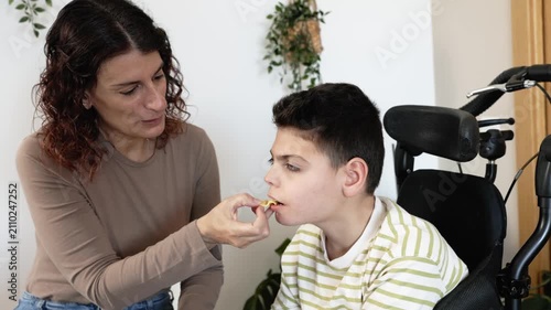 Loving mother feeding disabled son with cerebral palsy