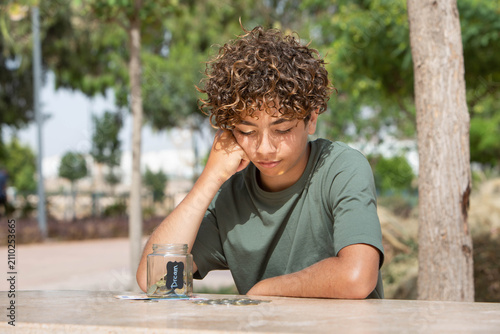 Фотография Thoughtful teenage boy counting coins and saving money outdoors, financial literacy concept