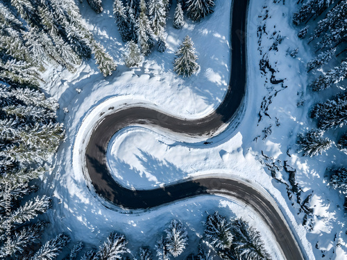 Aerial hairpin curve road through snowy forest with shadows
