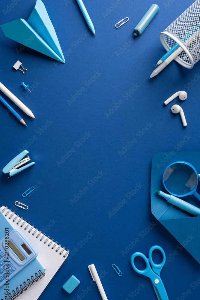 Fototapeta premium Back to school blue stationery flat lay with supplies and workspace on solid vertical blue background with empty space in the middle