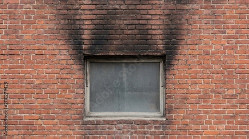 Scorched red brick wall with heavy black smoke stains and soot above a window after a fire