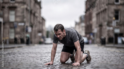 Exhausted Athlete Kneeling on Wet Street in Rain