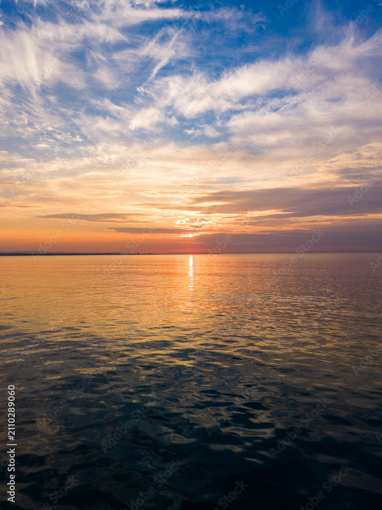 Obraz premium Sunset over the ocean with clouds and calm water in the evening sky near the coastline