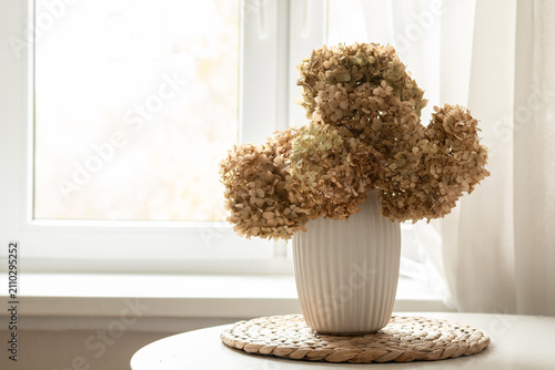 Dried hydrangea bouquet in white ceramic vase on bright window sill cozy autumn home decor