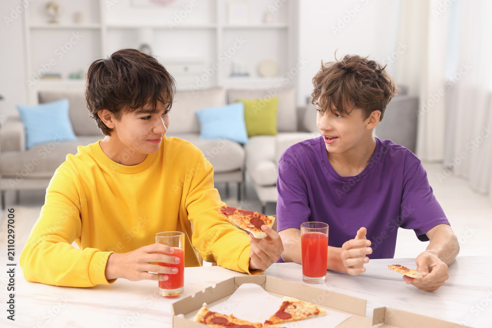 Obraz premium Teenage brothers eating pizza and drinking juice at white marble countertop at home
