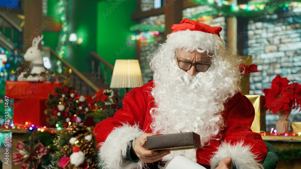 Fototapeta premium Santa Claus catches a gift box falling from above while reading children's letters as the present lands in his lap in a Christmas miracle scene.