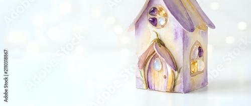 Whimsical purple and gold decorative birdhouse with glowing windows on soft bokeh background, suitable for holiday decor, seasonal marketing, and festive home design projects.