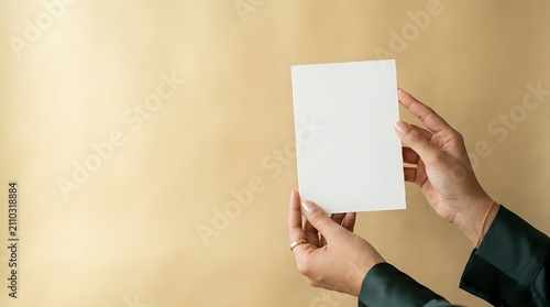 Hands holding blank white paper sheet against neutral beige wall background, mockup for branding, advertising, and marketing materials.