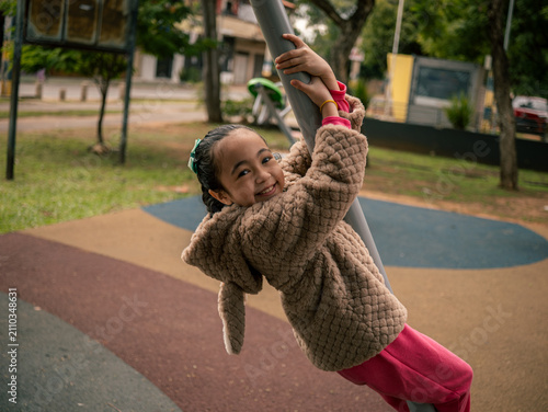 Child smiles while hanging on a playground pole