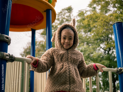 Kid in a fuzzy brown hooded coat with ears holds playground rails