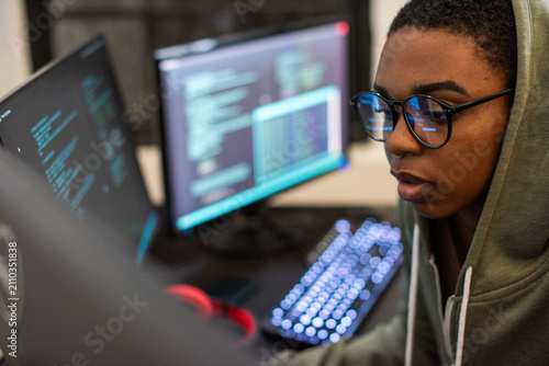 Quadro su tela Person in hoodie coding on dual monitors, focused and engaged.