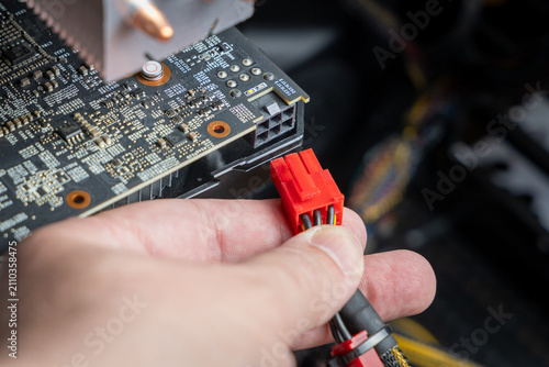 Technician connects a PCIe power connector to a budget graphics card. Repair and maintenance of personal computers