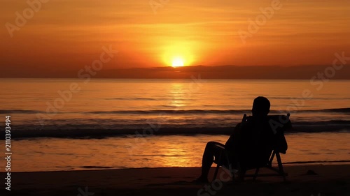 Silhouette of a person relaxing on a beach during sunset by the ocean.