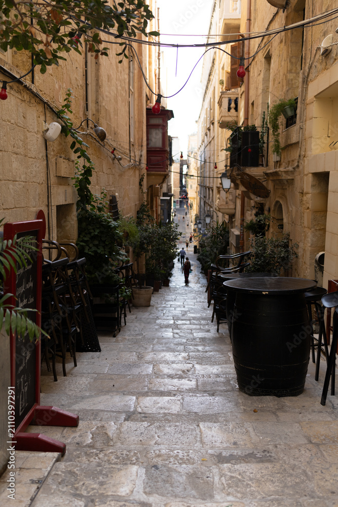 Fototapeta premium Empty outdoor bar terrace with wooden barrel tables on a narrow historic street in Valletta, Malta.