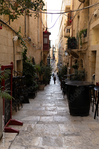 Empty outdoor bar terrace with wooden barrel tables on a narrow historic street in Valletta, Malta.