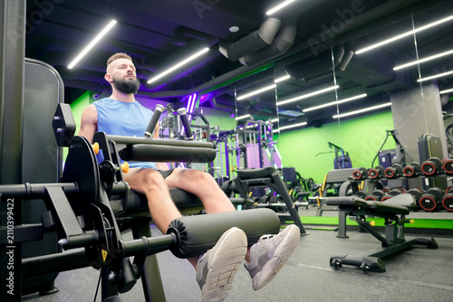 Athletic man performs leg extensions on a gym machine inside a modern fitness center at night, focusing on his quad muscles during a regular workout routine