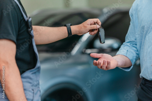 Mechanic handing over car key to satisfied customer after service at electric vehicle repair garage
