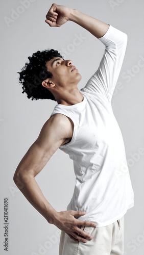 A young, athletic individual poses with one arm raised and bent, appearing to stretch. He wears a white shirt