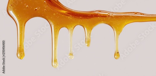 Close-up of a viscous, golden substance dripping against a neutral backdrop. The liquid forms teardrop-shaped drips. Small bubbles are visible