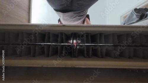 A ground view of a man using a brush tool to clean dust in a heating radiator.