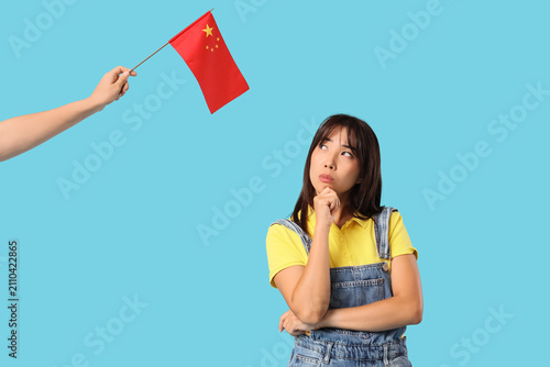 Thoughtful young Asian woman and hand with flag of China on blue background