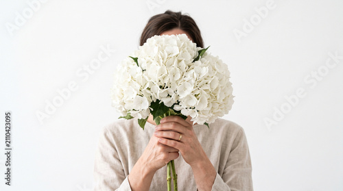 Front-facing studio portrait of a person holding a large white hydrangea flower in front of their face.