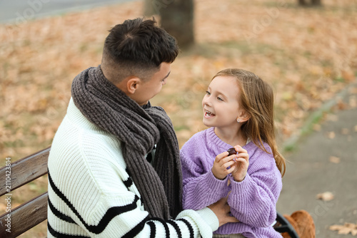 Happy father and his cute little daughter with chestnut sitting on bench in b...
