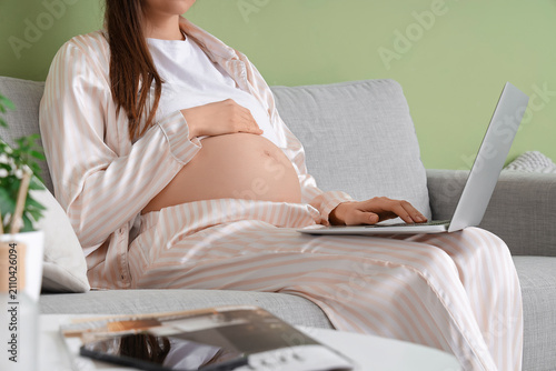 Pregnant businesswoman in pajamas working with laptop on sofa at home, closeup