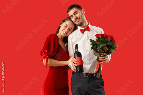 Happy young couple with bottle of wine and roses on red background. Valentine...