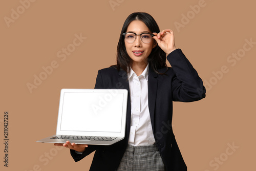 Portrait of young Asian businesswoman holding modern laptop with blank screen...