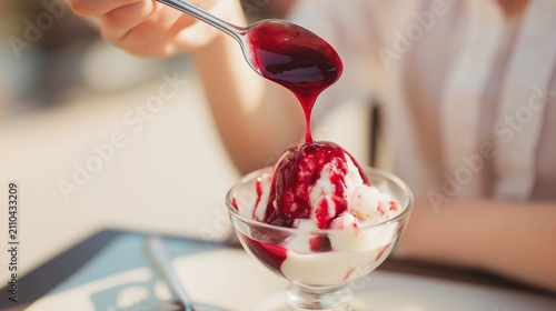 Female hands slowly pouring berry sauce over vanilla ice cream